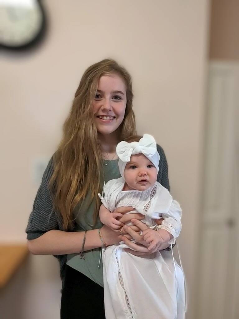 Young woman smiling while holding a baby in a white dedication gown