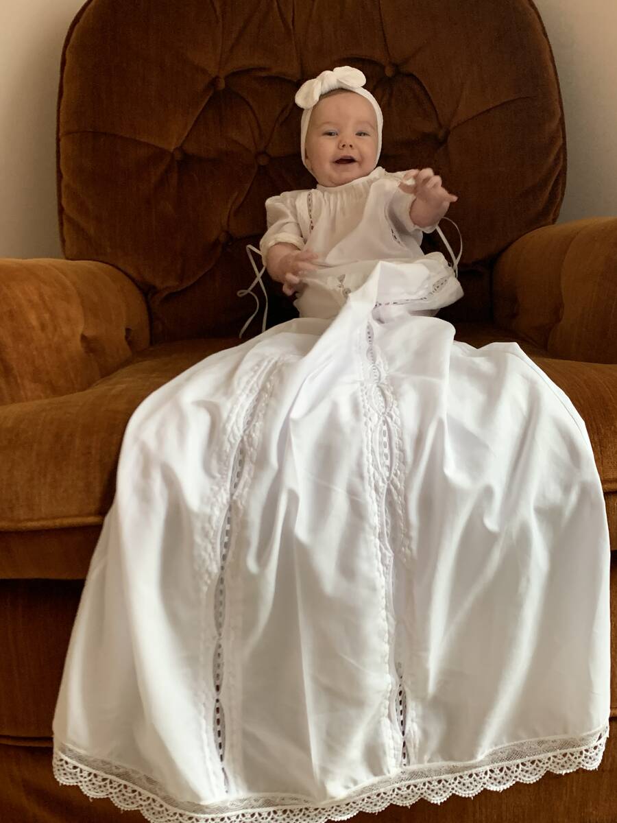 Baby in a white christening gown sitting in a leather chair