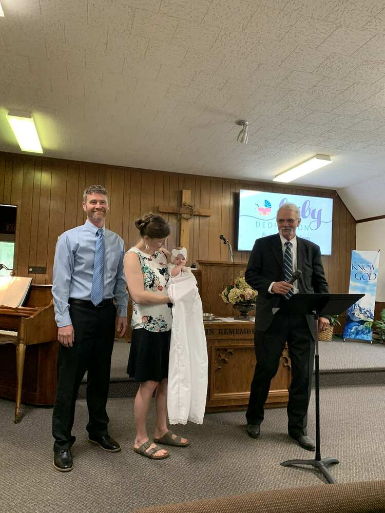 Parents holding their baby beside the pastor at the pulpit
