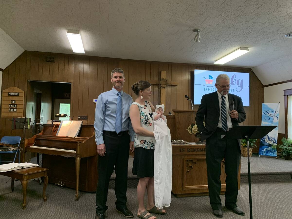 Family standing with the pastor at the front of the sanctuary during a baby dedication