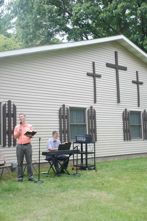Pastor preaching outdoors beside the church with a keyboard player