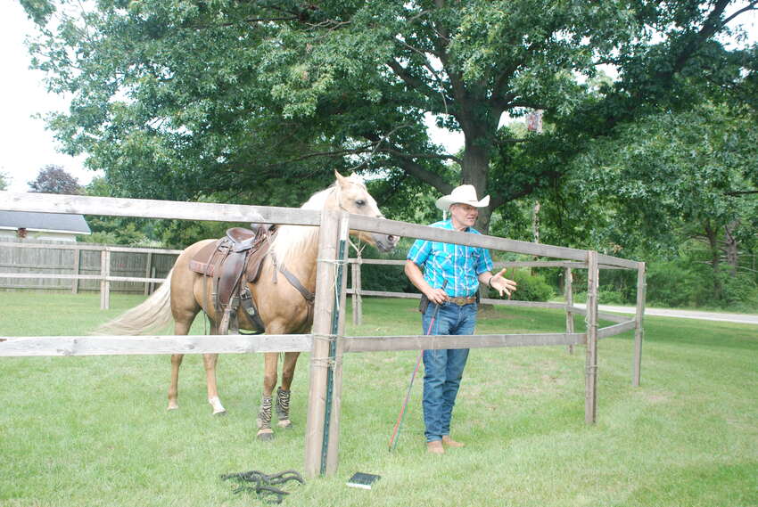 Horseman in a cowboy hat standing with a palomino horse at the fence