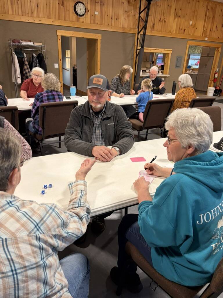 Friends of all ages playing a dice game at tables in the fellowship hall